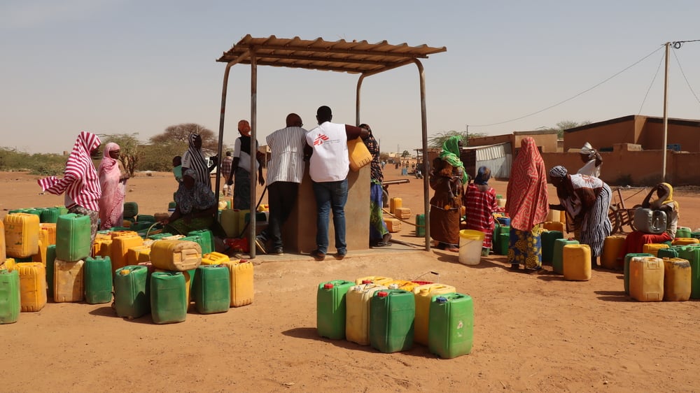 Nuestro personal ayuda a las personas desplazadas a recoger agua limpia en un punto de agua en el distrito de Gorom Gorom, en la región desértica del Sahel, al norte de Burkina Faso. Febrero de 2021