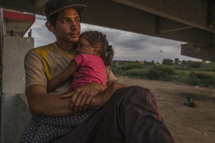 Un migrante venezolano y su hija se toman un momento de descanso cerca del Río Tumbes, Perú.