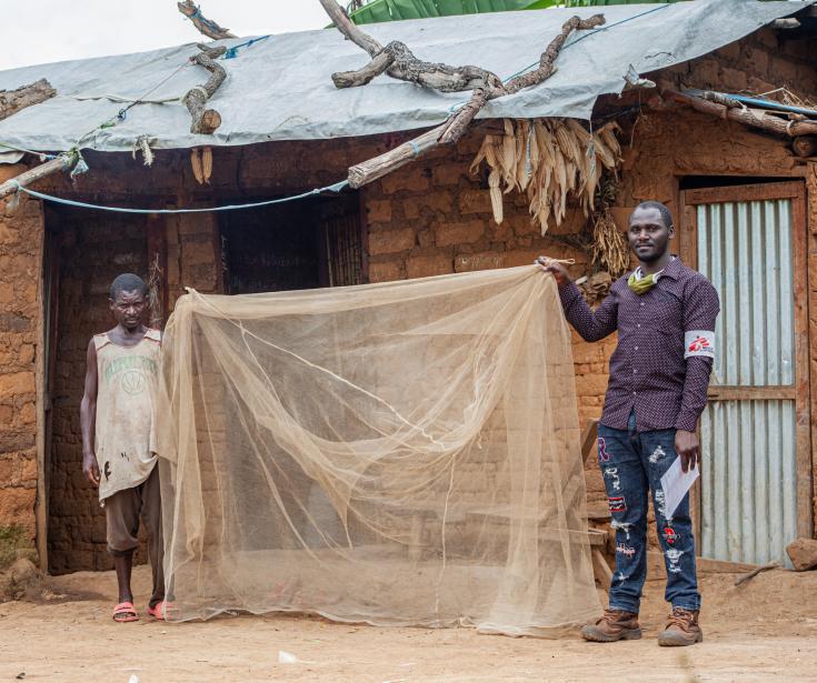 Sibomana Louis, un refugiado burundés que vive en el campamento de Nduta desde 2015, sostiene el mosquitero que recibió de MSF con Fulgence Irakoze, supervisor de control de vectores de MSF. 