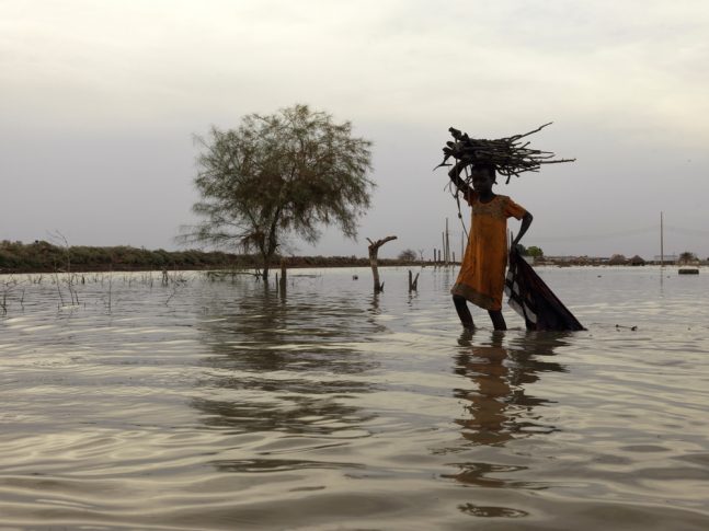 Una niña camina entre las aguas de la inundación mientras carga leña para su hogar en Rubkona, Sudán del Sur. Peter Caton.