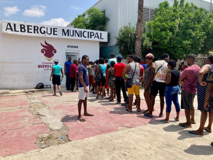 Personas migrantes aguardando en la entrada de un albergue en Nuevo Laredo, México