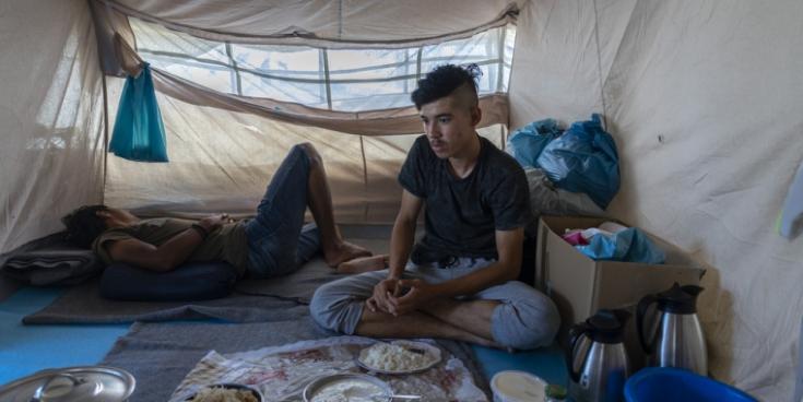 Dos jóvenes afganos sentados en una tienda de campaña que deben compartir con familias desconocidas para ellos en el Olive Groove cercano al campo de Moria, en la isla de Lesbos.